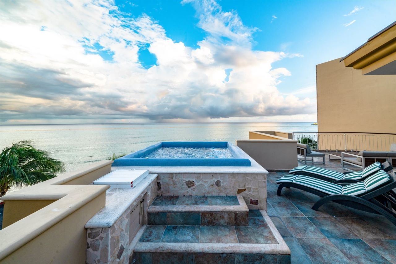 Rooftop with a small pool, lounge chair, ocean view under a cloudy sky.