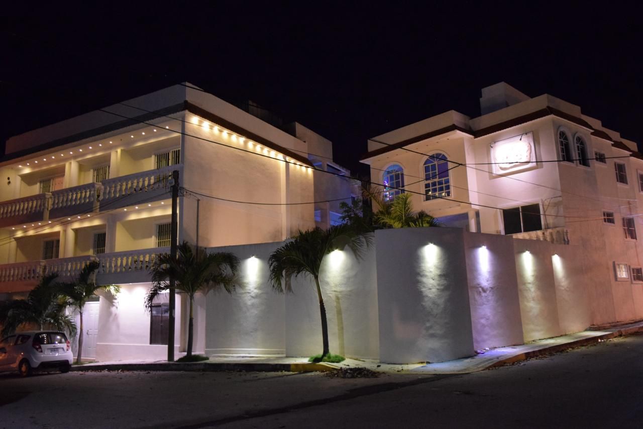 White building lit up at night, palm tree in front, street and sky visible.
