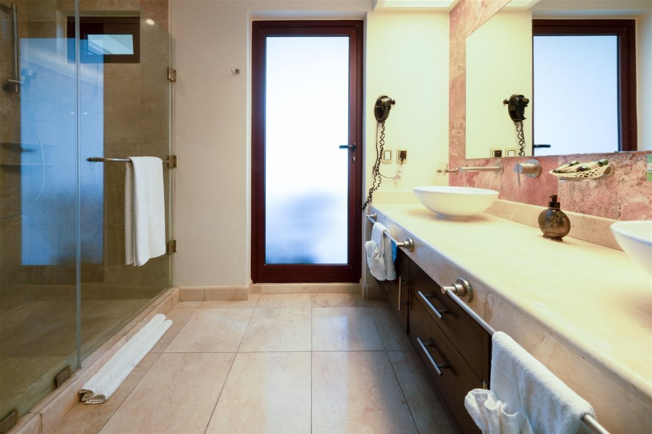 Bathroom with glass shower, frosted door, double sink, and stone floor.