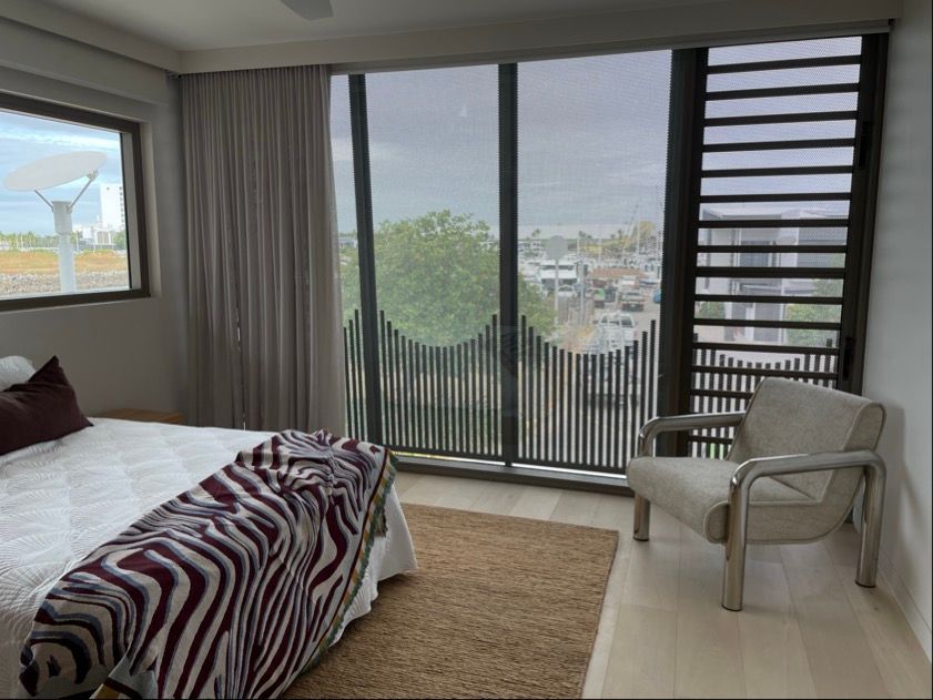 Bedroom with a large window, beige chair, bed with zebra-striped blanket, and a view of a cityscape on a cloudy day — Lifestyle Aluminium Lattice in West End, QLD