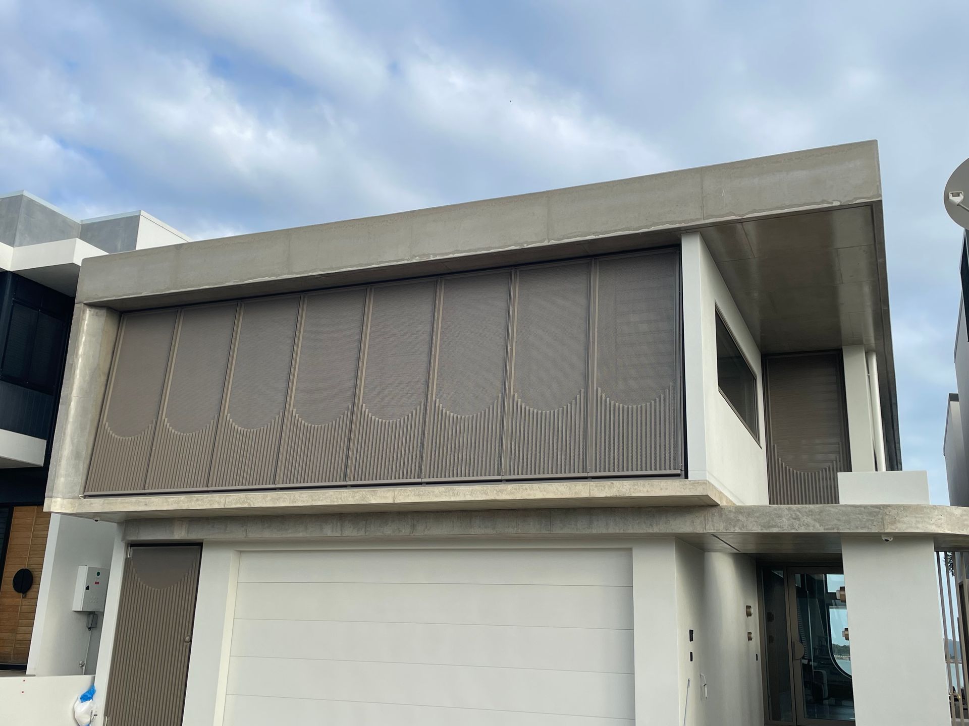 Modern two-story home with a garage. Gray, textured siding covers the upper level. White garage door. Cloudy sky — Lifestyle Aluminium Lattice in West End, QLD