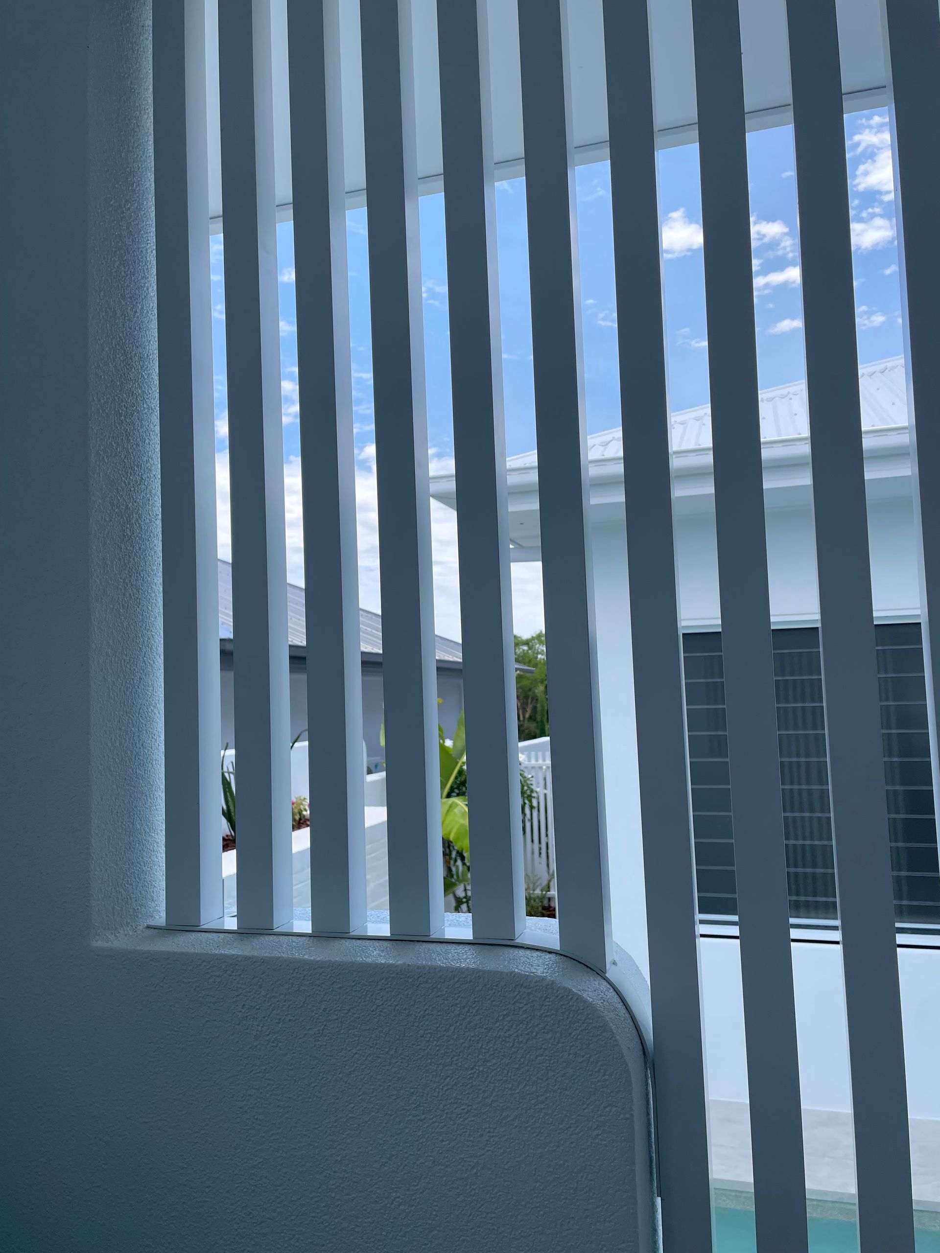 White vertical slats frame a view of a bright blue sky and a white building with a pool — Lifestyle Aluminium Lattice in West End, QLD