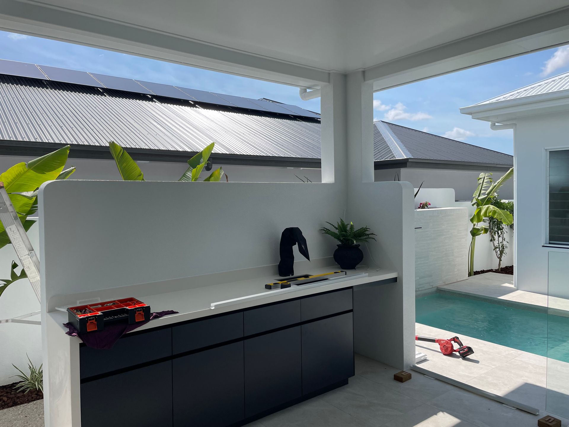 Outdoor kitchen with dark cabinets, white countertop, pool, and blue sky — Lifestyle Aluminium Lattice in West End, QLD