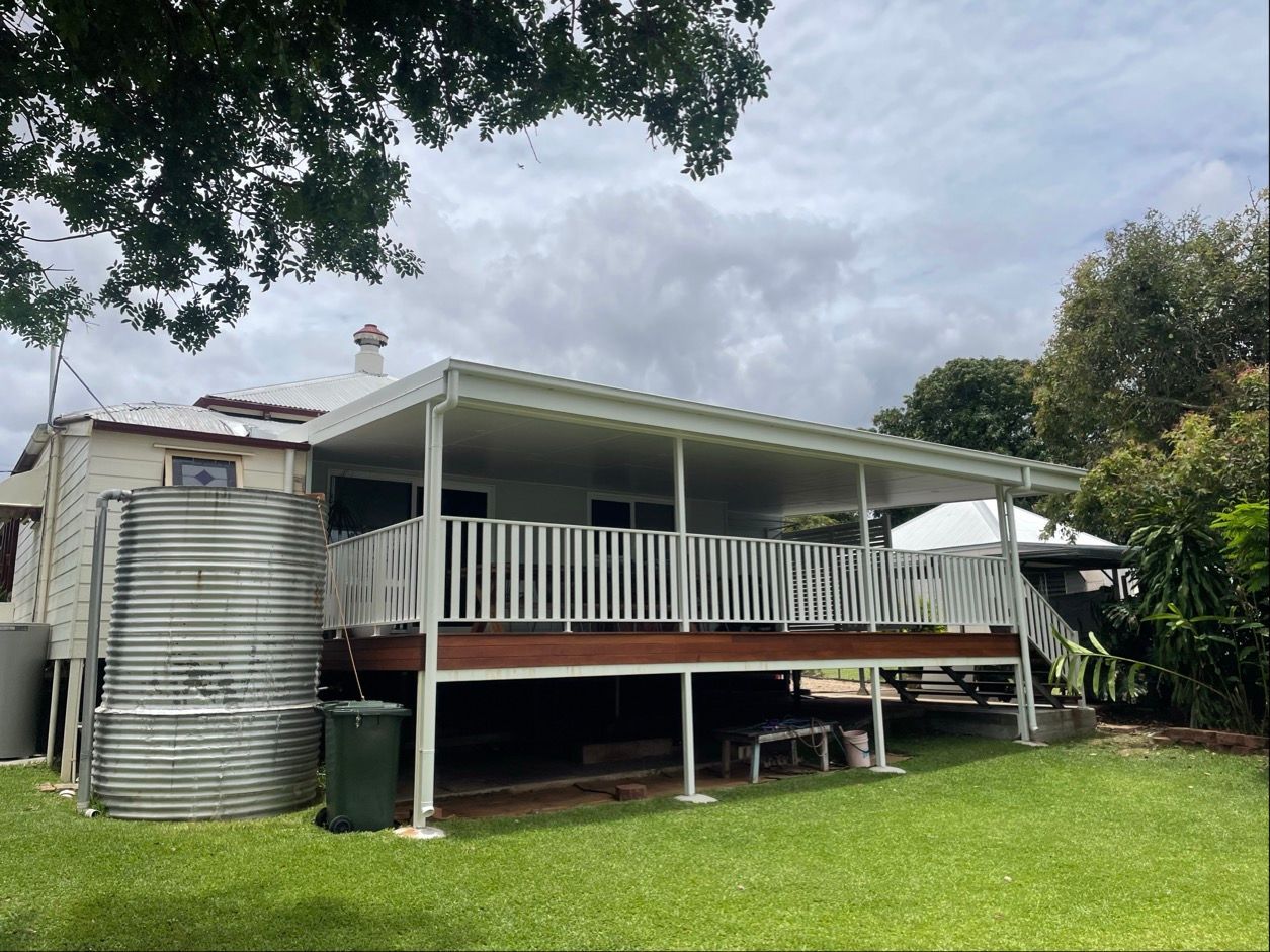 A weathered, one-story house with a covered porch, water tank, and green lawn on a cloudy day — Lifestyle Aluminium Lattice in West End, QLD