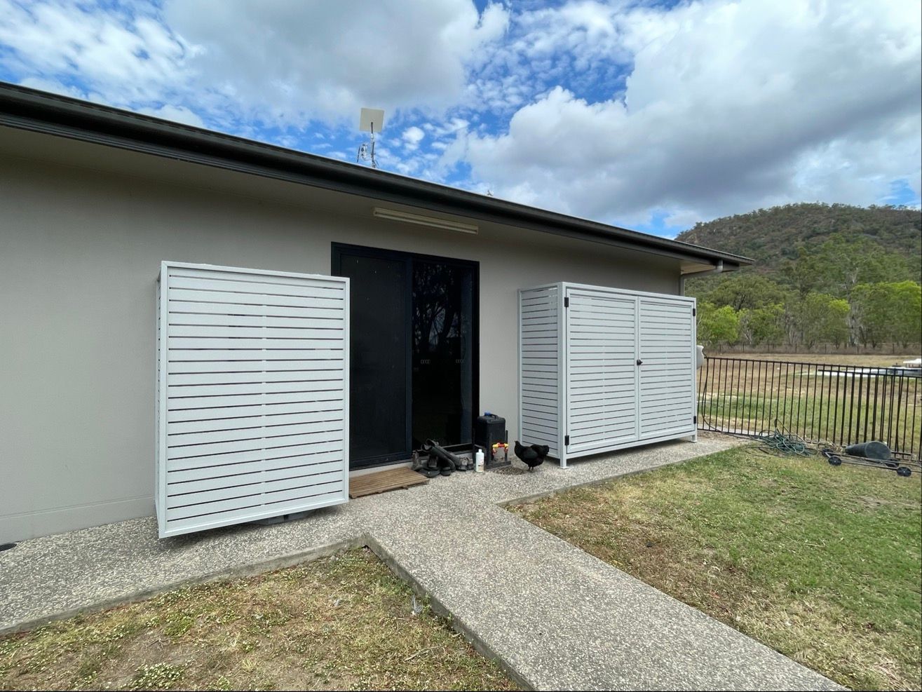 Grey house with decorative side panels next to black door, path leading to it, chickens nearby, mountains in background — Lifestyle Aluminium Lattice in West End, QLD