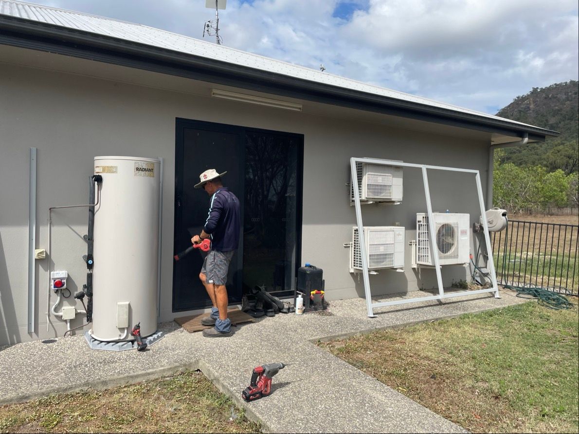 Man working on a building exterior with a water heater and air conditioning units. Outdoor setting — Lifestyle Aluminium Lattice in West End, QLD