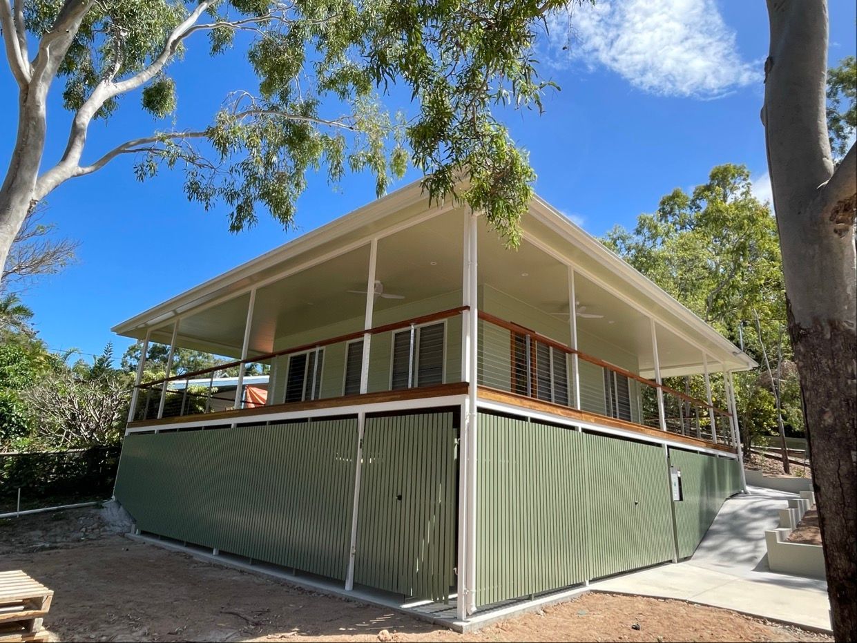 Green and white building with a wrap-around porch under a bright blue sky.