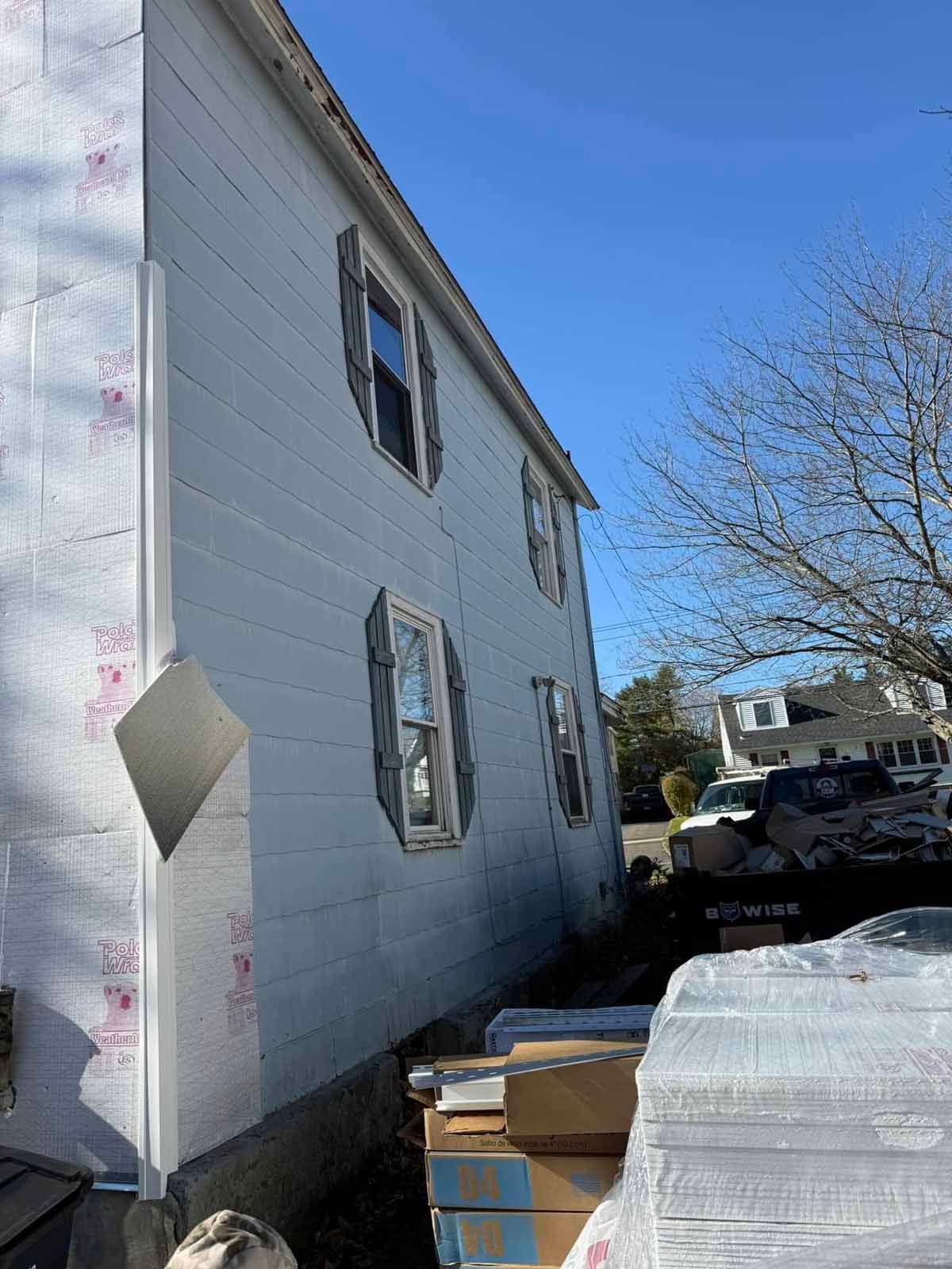 Side view of a white house under construction with stacked materials and a parked car beside it.