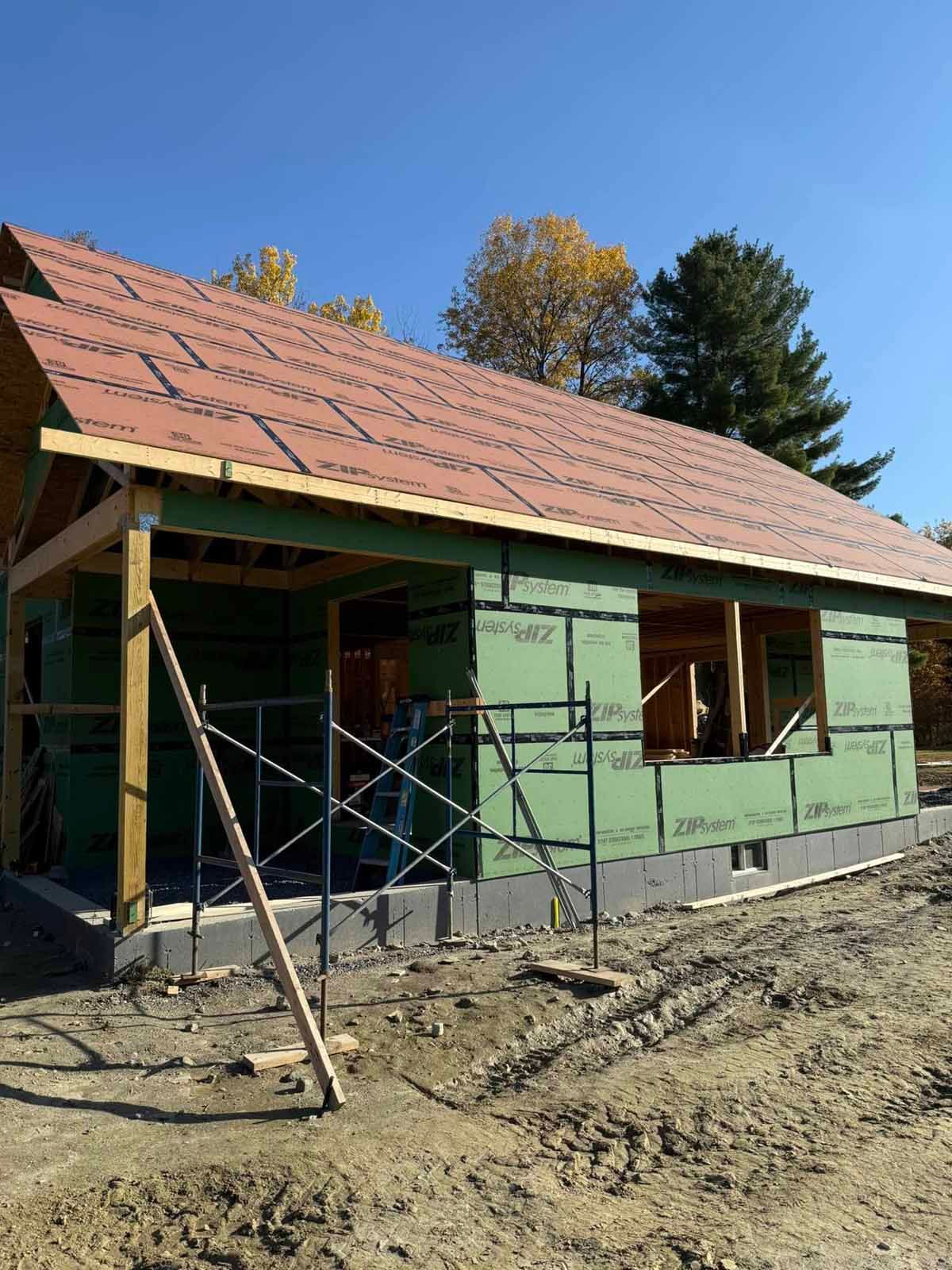 Partially built green house with scaffolding and exposed roof framing on a dirt lot in daylight
