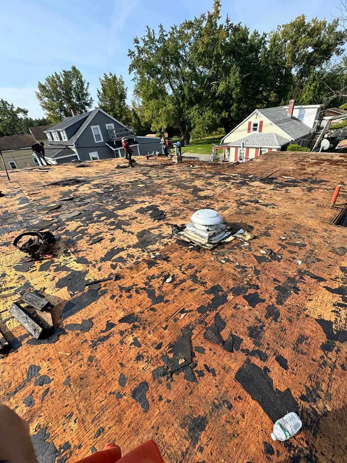 Damaged roof with tar paper exposed, vents and debris, viewed from above in a residential neighborhood