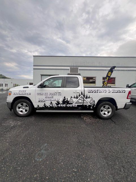 White pickup truck with a mountain landscape wrap parked in front of a building under cloudy skies