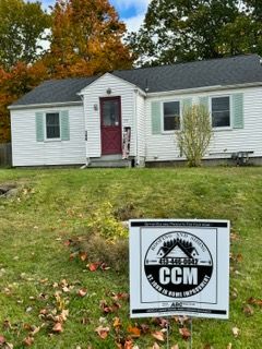 Small white house with red door and front lawn; CCM sign in the yard.