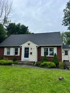 Small brick ranch house with a white front door, dark roof, and star decoration, seen from a green lawn.