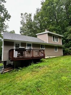 Two-story house with brown siding, white trim, and a wooden deck on a grassy slope.