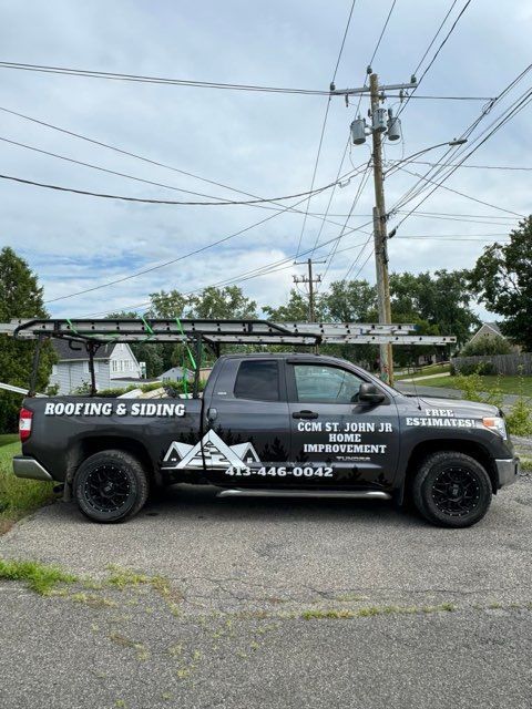 Black roofing and siding pickup truck parked outdoors on gravel under power lines.