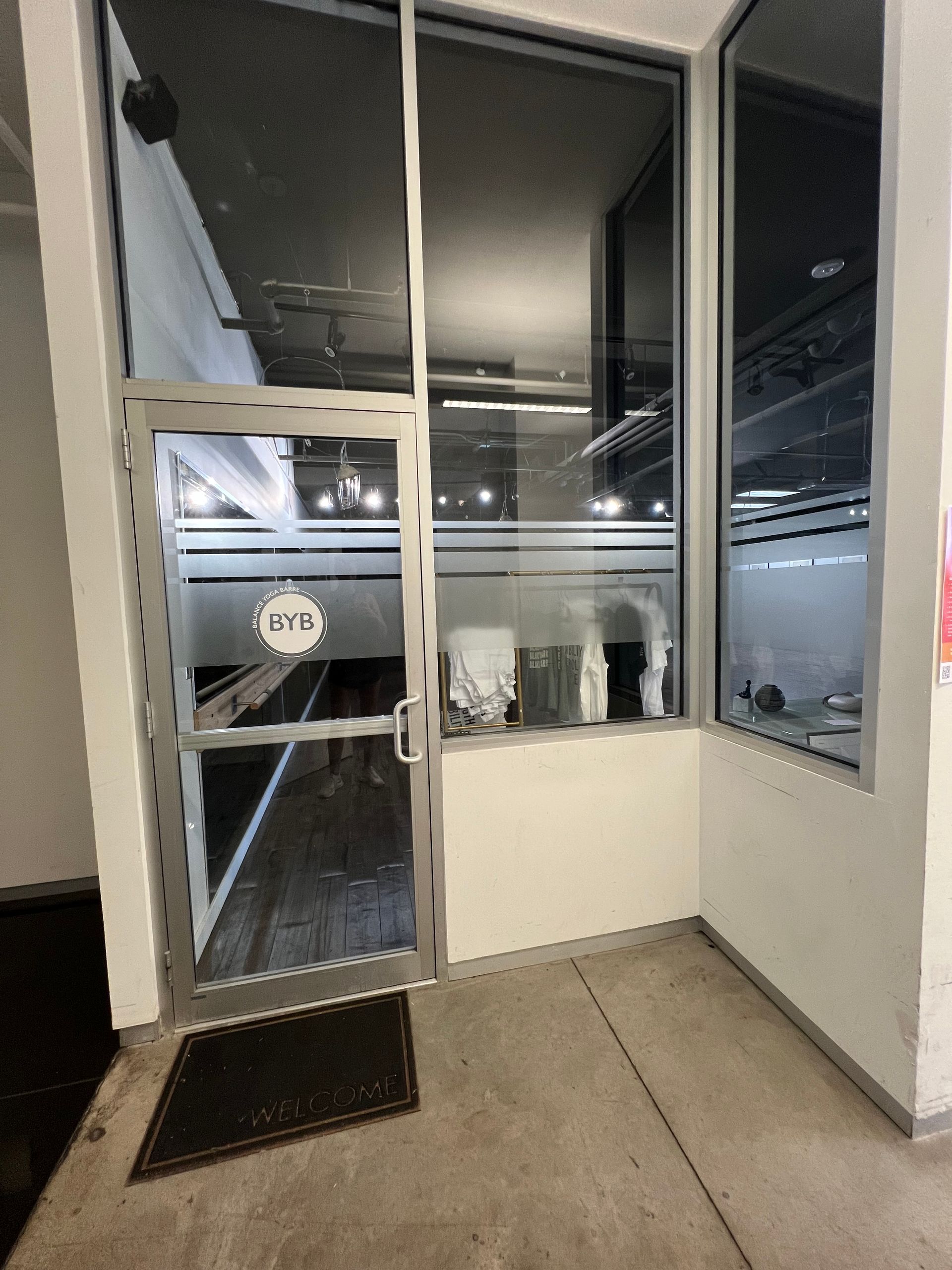 An exterior entrance to a modern storefront with a glass door and window panels featuring the 