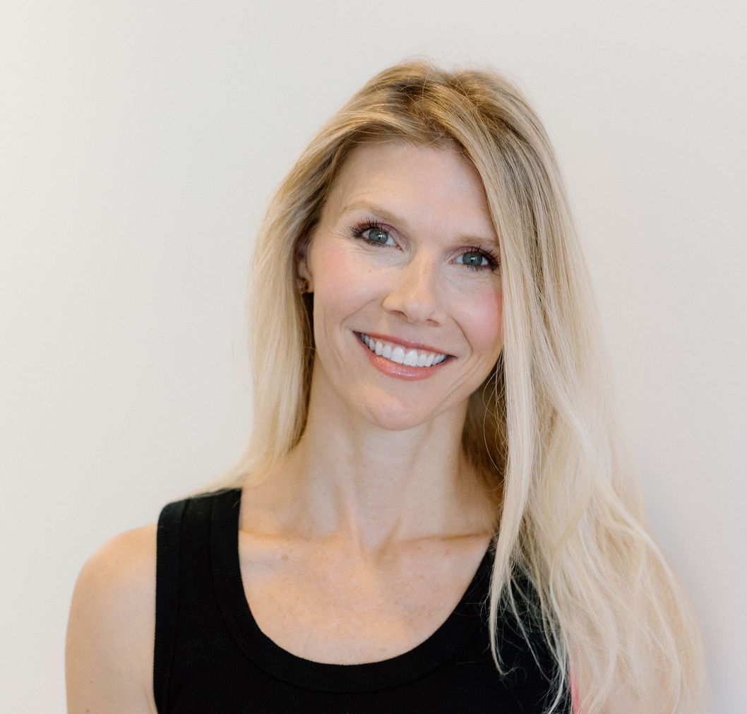 A woman with long blonde hair and a friendly smile, wearing a black tank top against a plain white background.