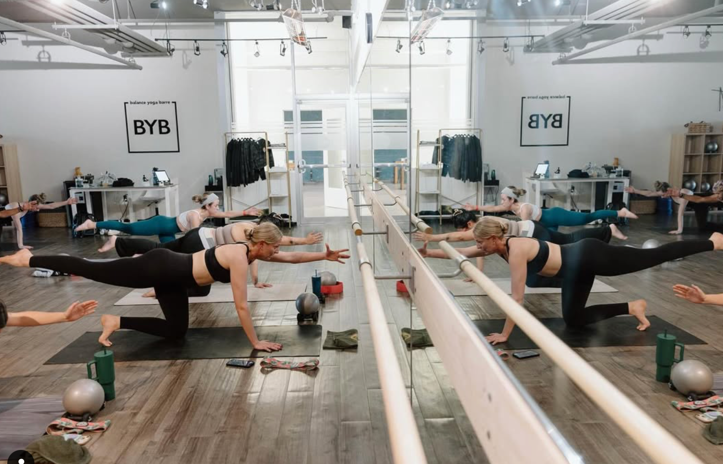 Participants in a bright studio exercise on mats, extending one arm and opposite leg while balancing on hands and knees.