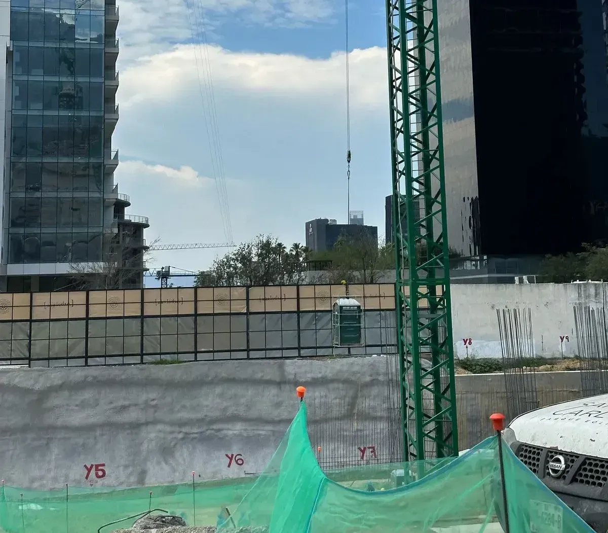 Una obra en construcción con una valla y una grúa al fondo usando una jaula para baño portátil