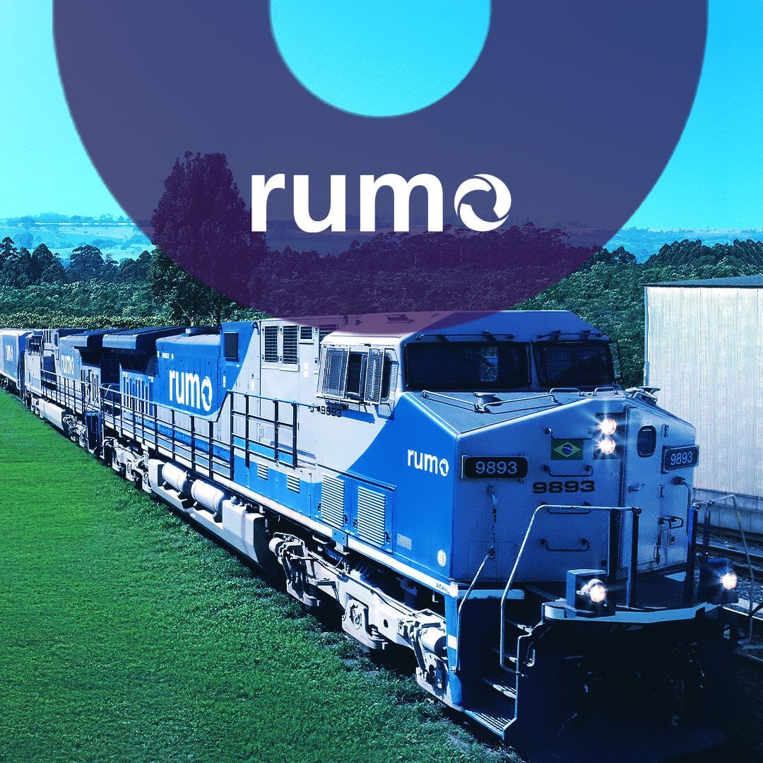 Um comboio de trens azuis e brancos está descendo os trilhos, com logo da Rumo.