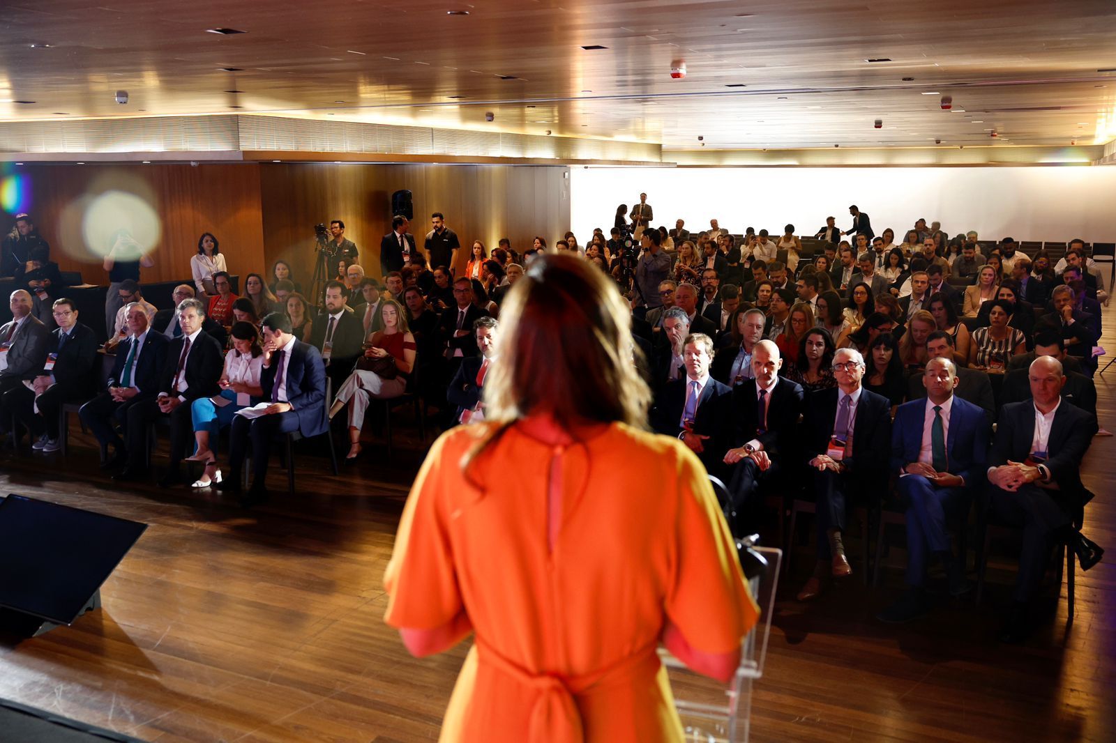 uma mulher com um vestido laranja está em um pódio na frente de uma multidão.