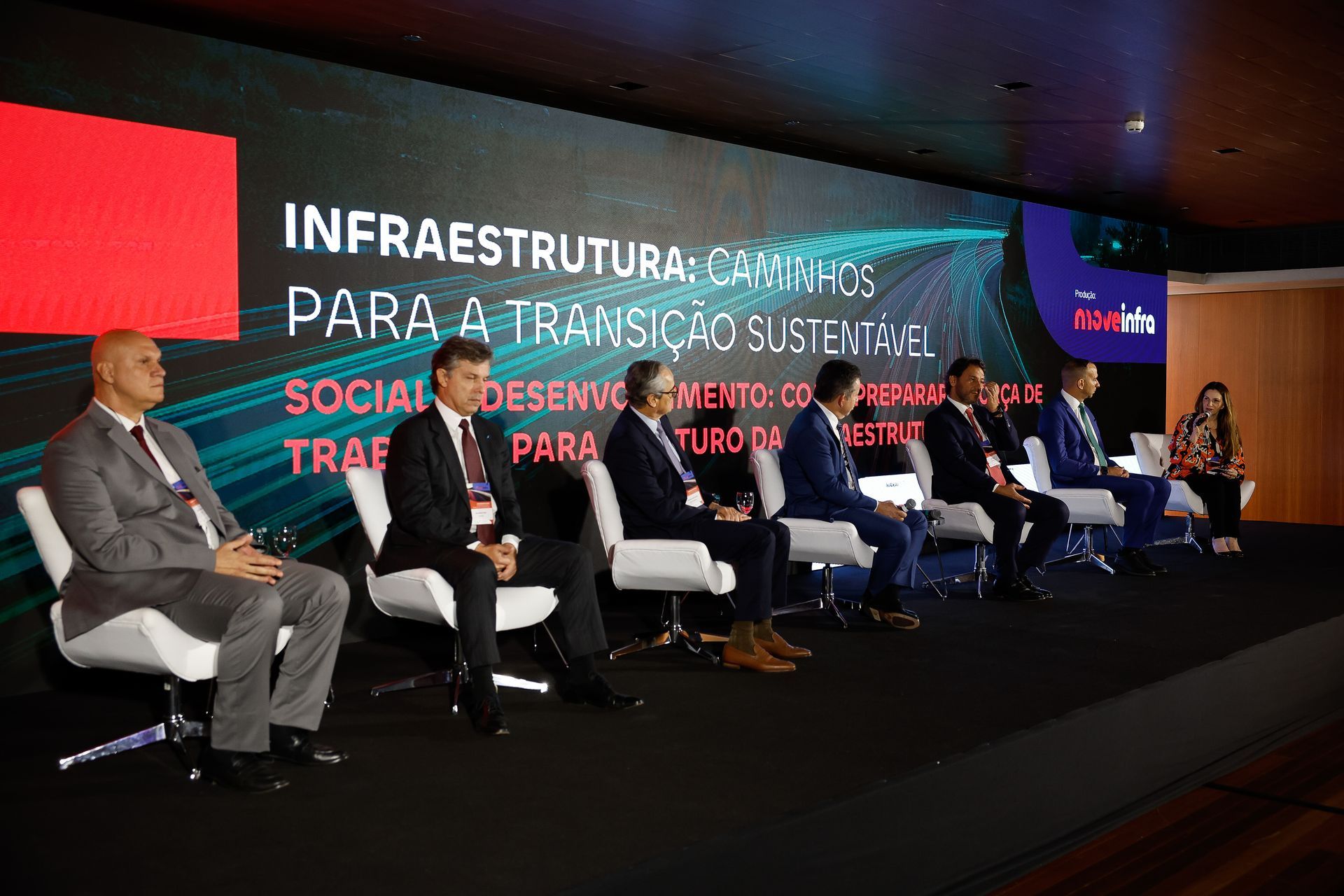 Um grupo de pessoas está sentado em cadeiras em frente a uma grande tela.