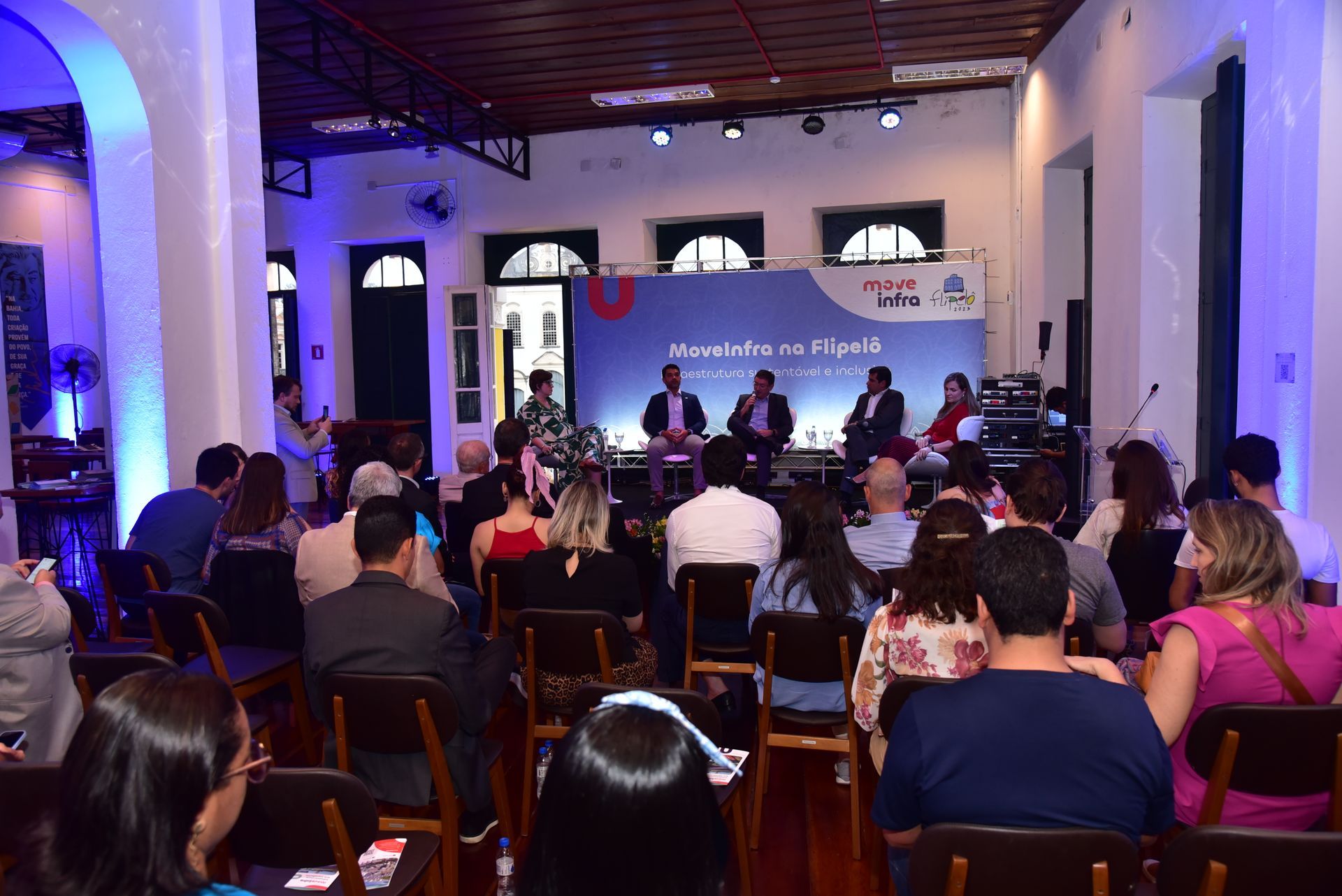 Um grupo de pessoas está sentado em cadeiras em uma sala assistindo a uma apresentação.