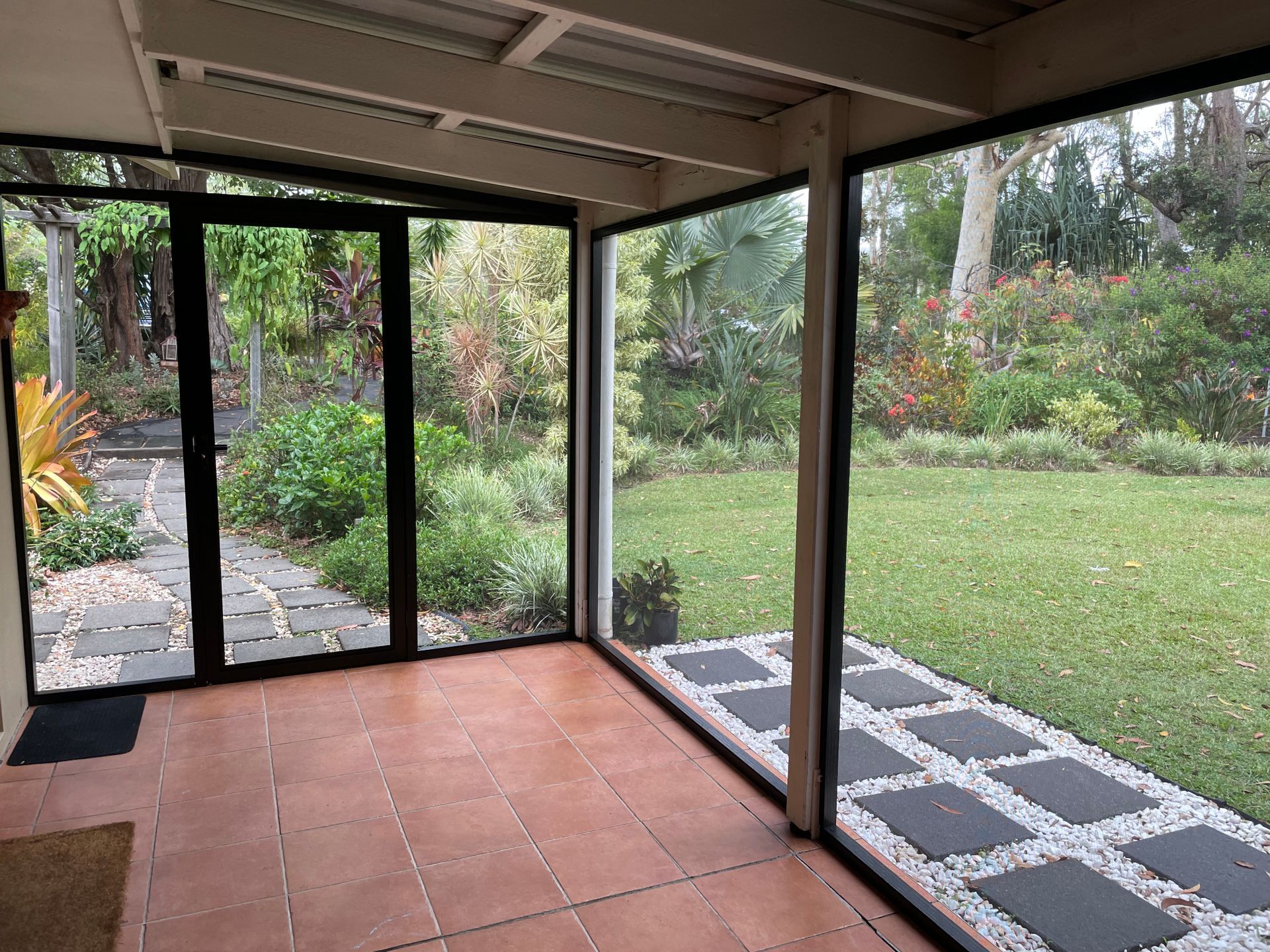 Image of a patio on a house screened with stainless steel mesh with side door and a view of the back garden & lawn