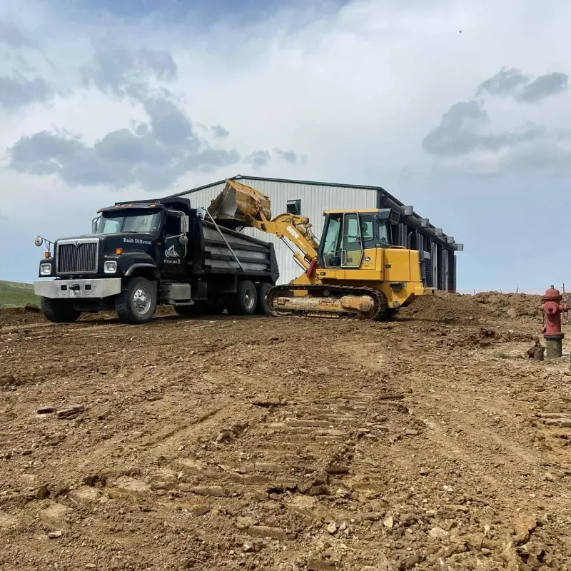 A dump truck is parked next to a bulldozer in a dirt field.