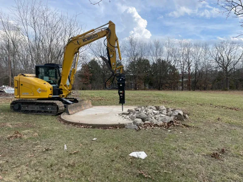 A yellow excavator is digging a hole in the ground in a field.