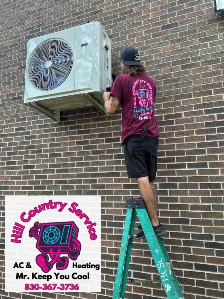 A man is standing on a ladder fixing an air conditioner on a brick wall.