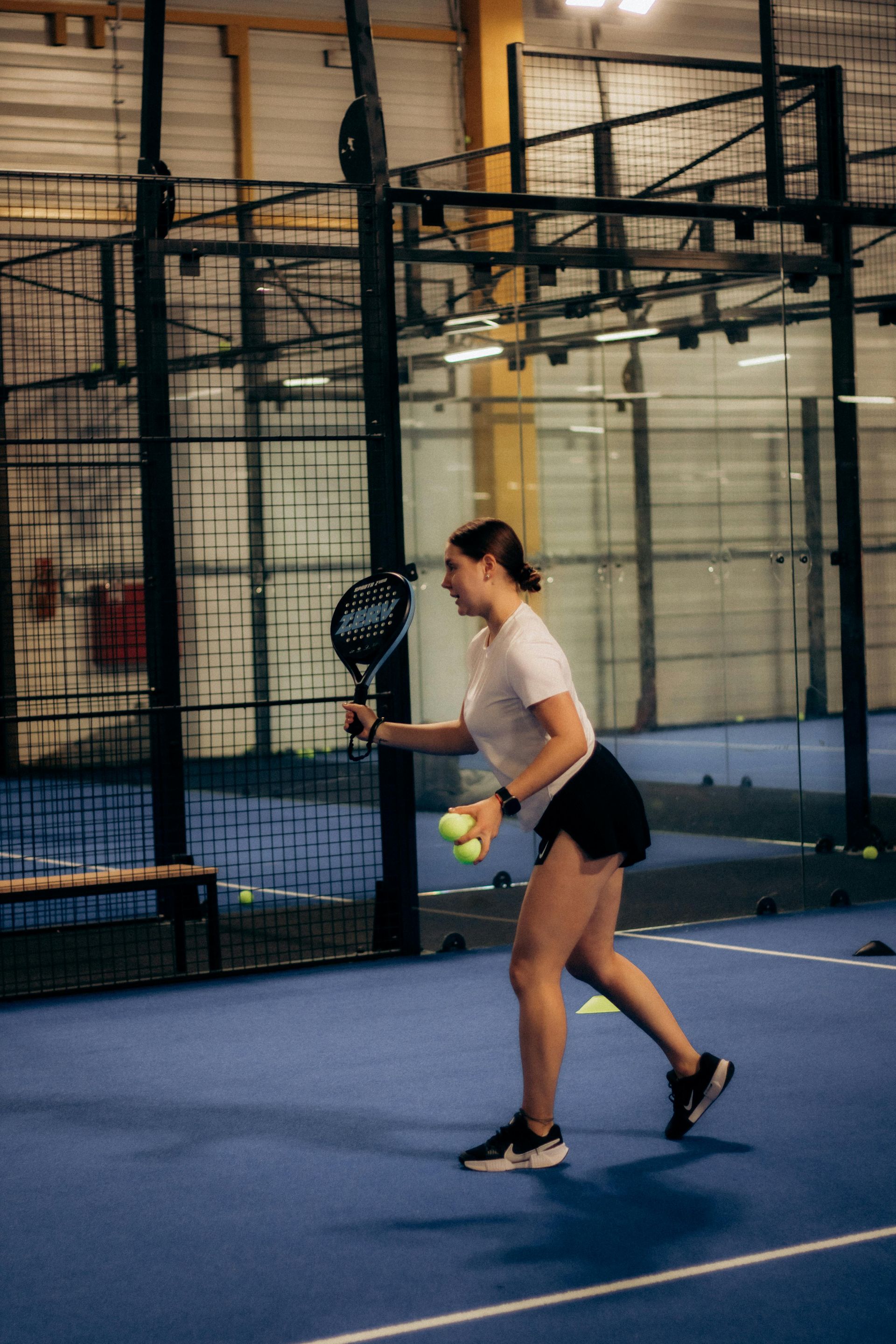 Woman playing tennis on an indoor court, mid-swing with a racket and ball in hand.