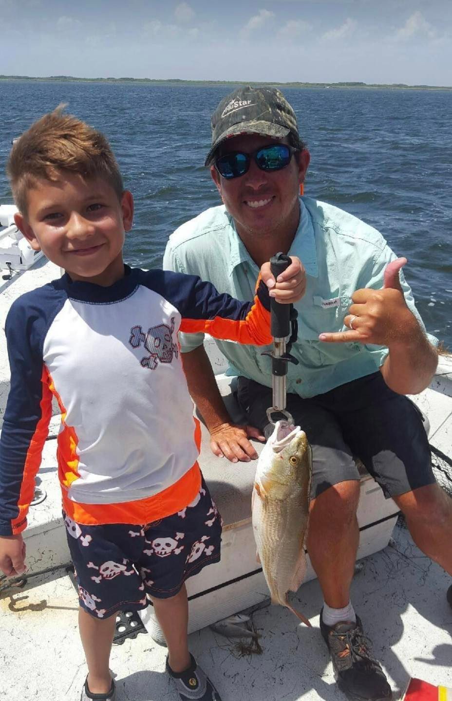 A man and a boy on a boat holding a fish