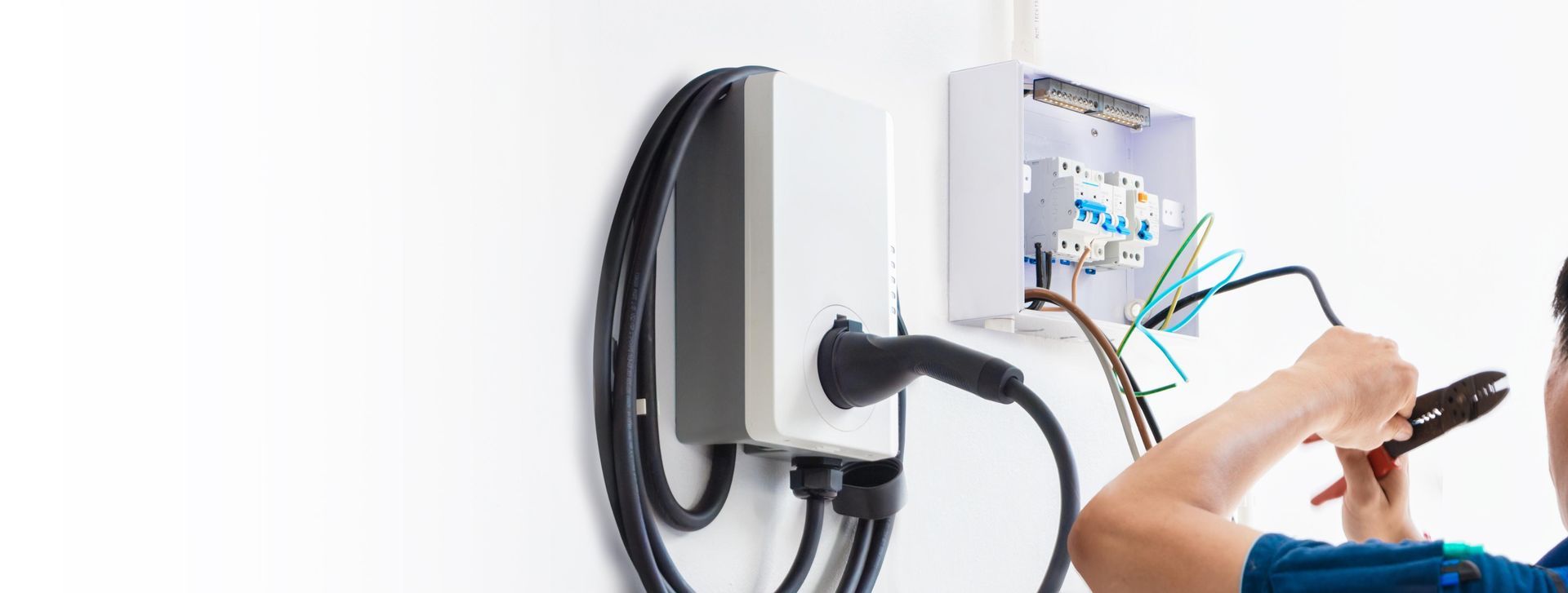 Person charging an electric vehicle with a wall-mounted charging station and cable