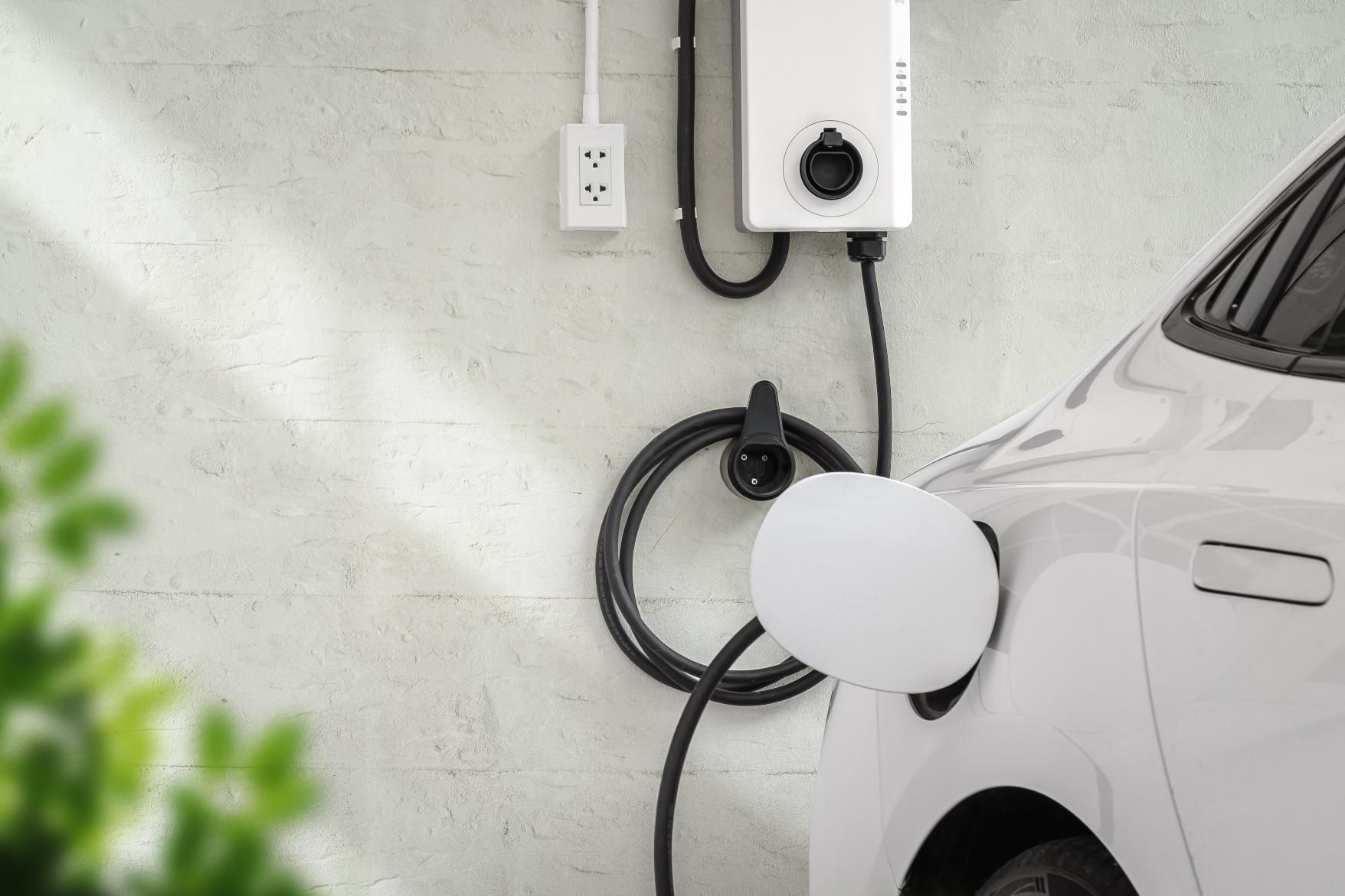 White electric car charging beside a wall-mounted EV charger in a garage