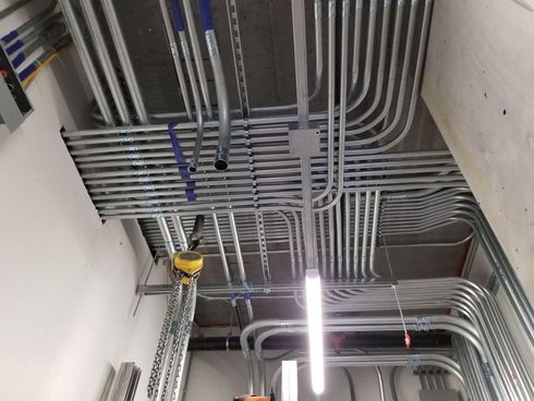 Ceiling with exposed gray electrical conduits and bright fluorescent light in a utility space