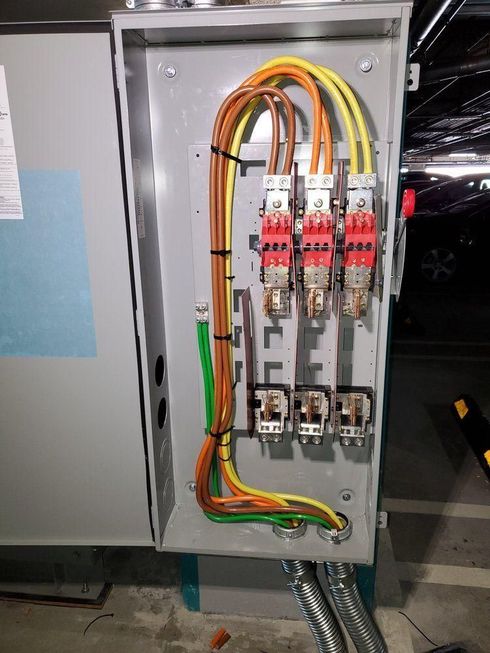 Open electrical panel with colored wires, breakers, and cables mounted inside a gray cabinet.