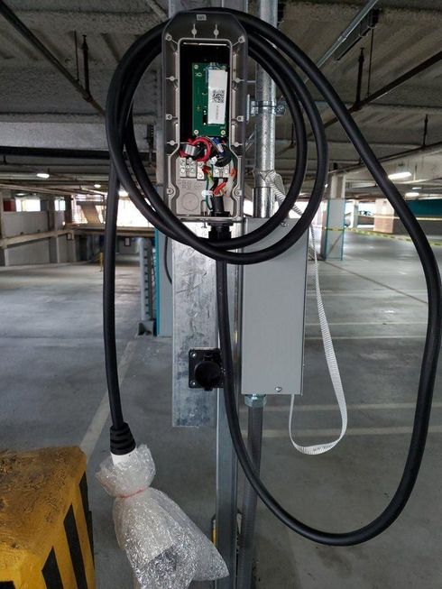 Electrical control panel mounted on a concrete pillar with coiled black cables in a parking garage.