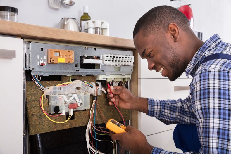 Technician inspecting wiring inside an open electrical control panel with a multimeter