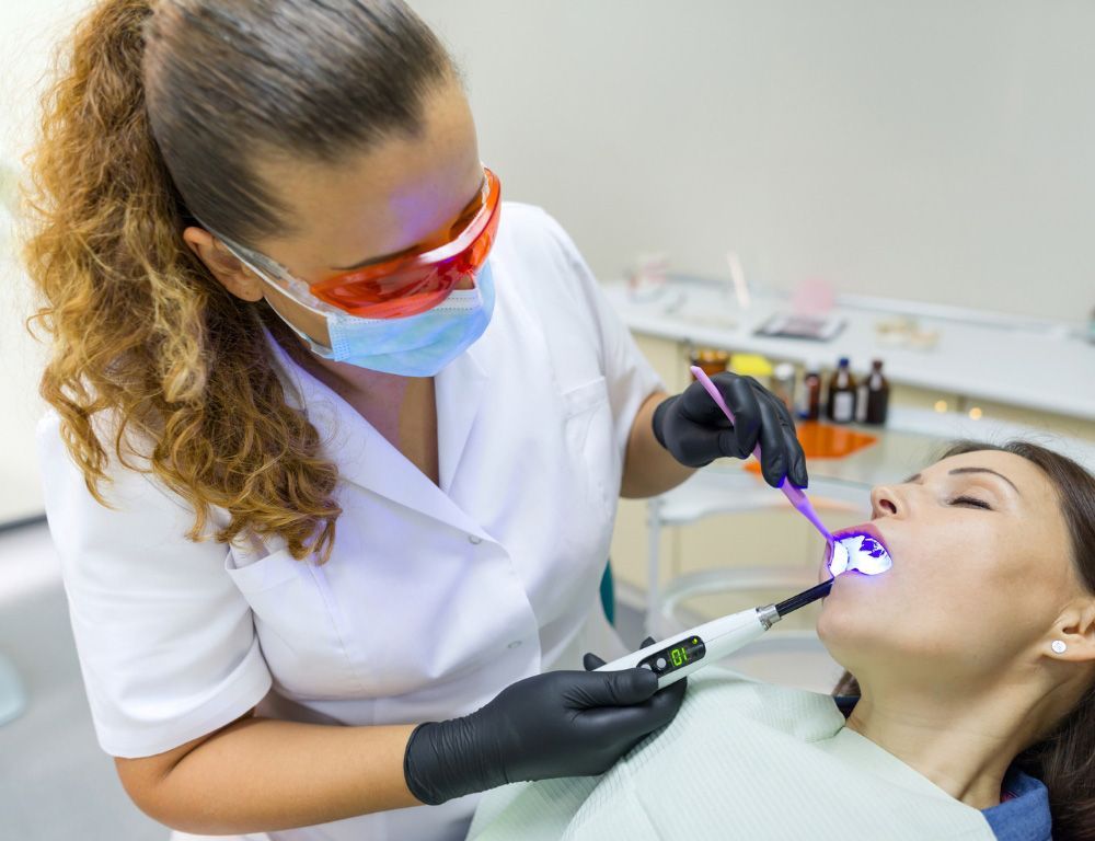 A woman is getting her teeth whitened by a dentist in a dental office.