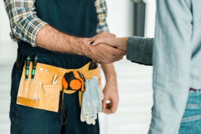 Una persona in abiti da lavoro stringe la mano a una persona con un maglione grigio e jeans.