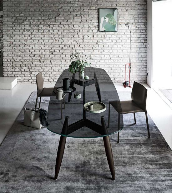 Moderna sala da pranzo con tavolo in vetro, due sedie, tappeto e parete in mattoni.