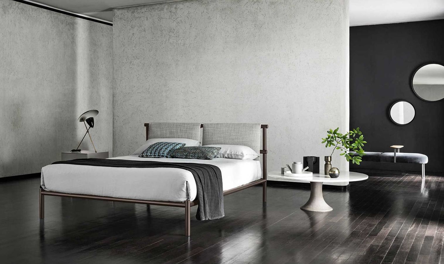 Camera da letto moderna con letto, tavolino, pavimenti scuri e specchi decorativi.