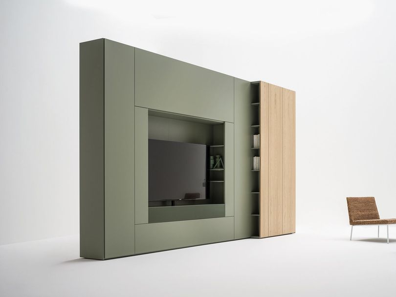 Mobiletto modulare verde per l'intrattenimento con TV, spazio per riporre oggetti e un mobiletto in legno chiaro. Una sedia è posizionata sulla destra.