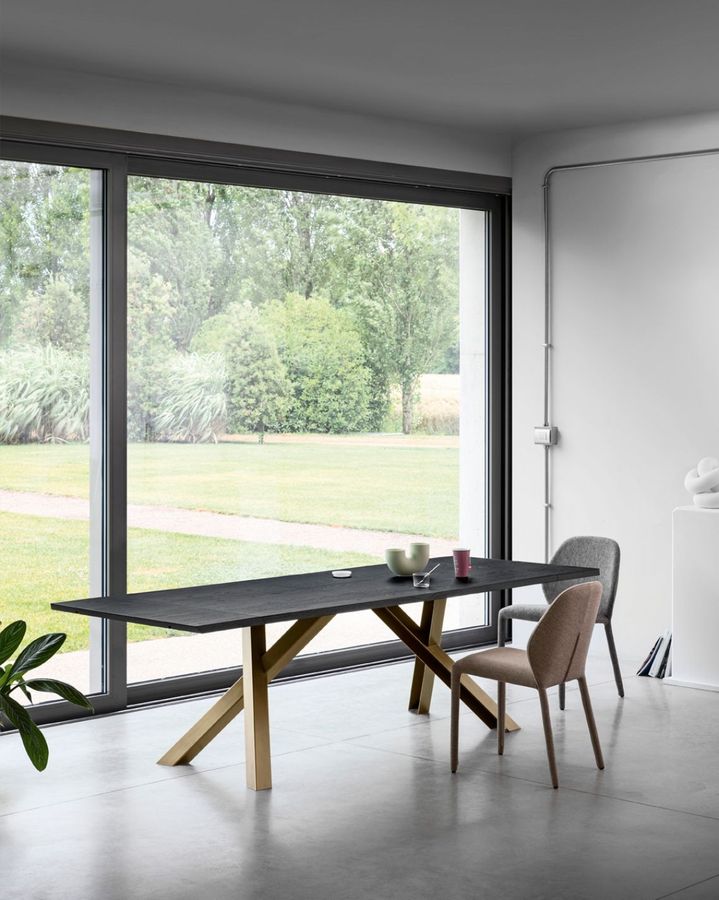 Tavolo da pranzo con piano scuro e gambe dorate, due sedie e ampia finestra con vista sull'esterno.