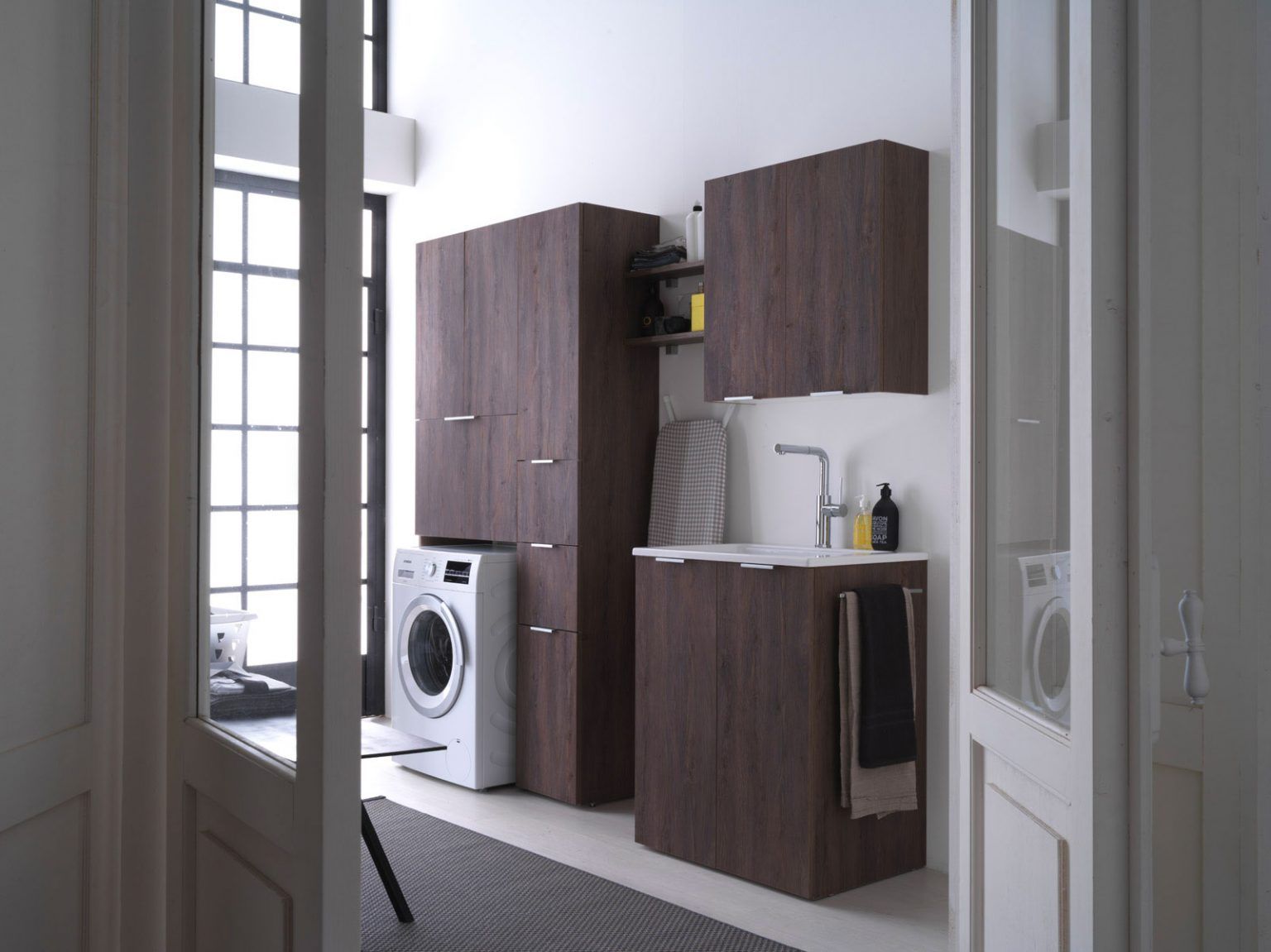 Lavanderia con mobili in legno scuro, lavatrice, lavandino e finestra.