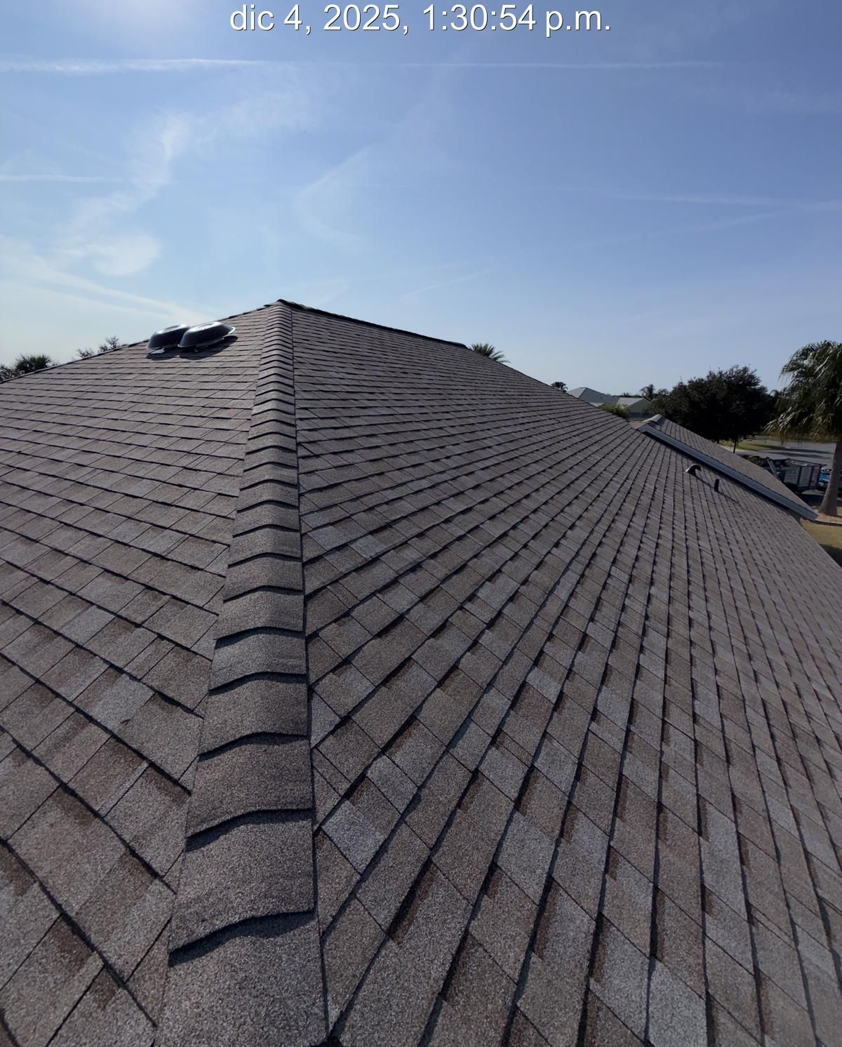 Roof of a house with gray shingles against a clear, blue sky.