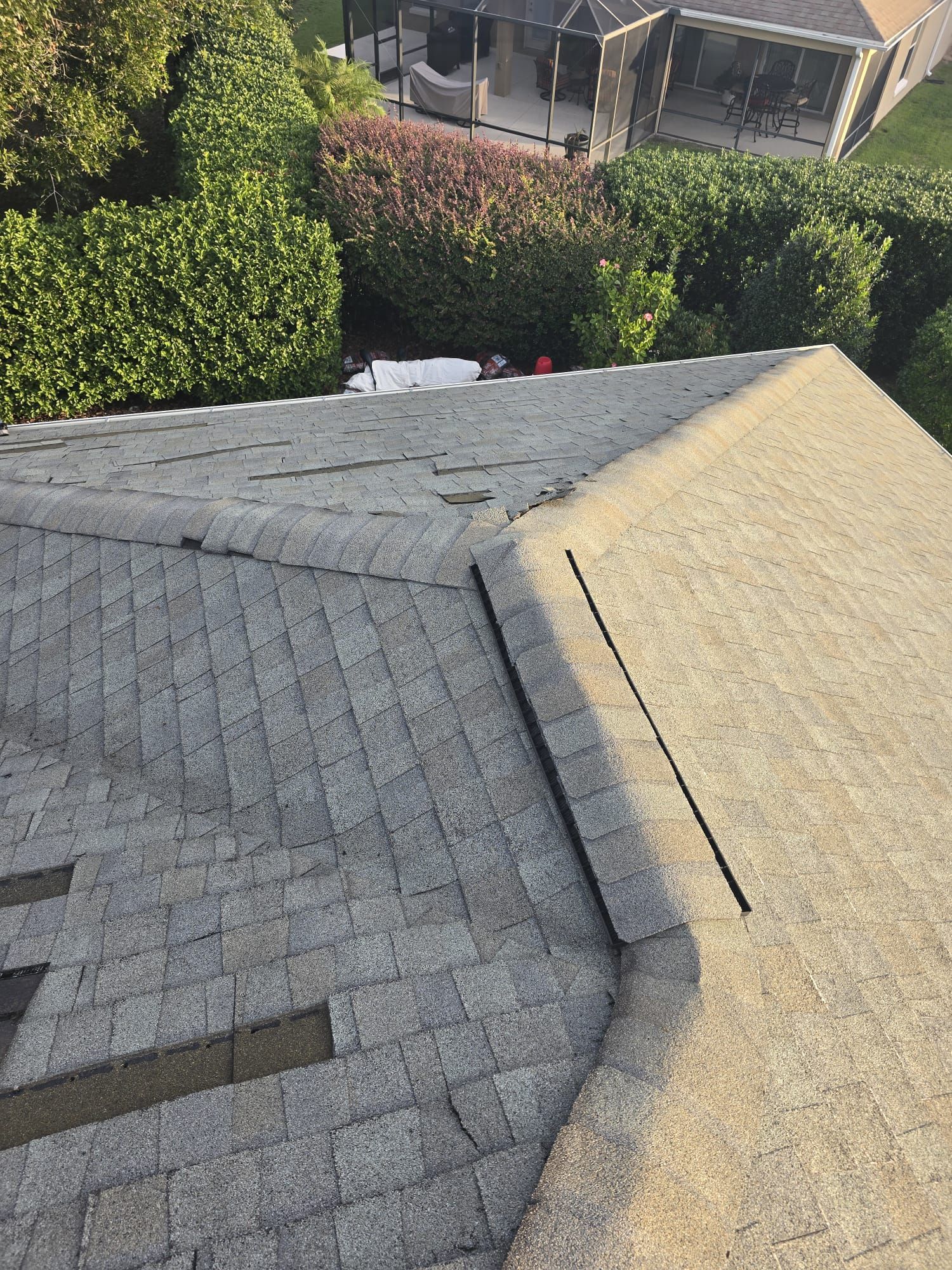 Overhead view of a roof with missing shingles and a ridge vent, surrounded by greenery.