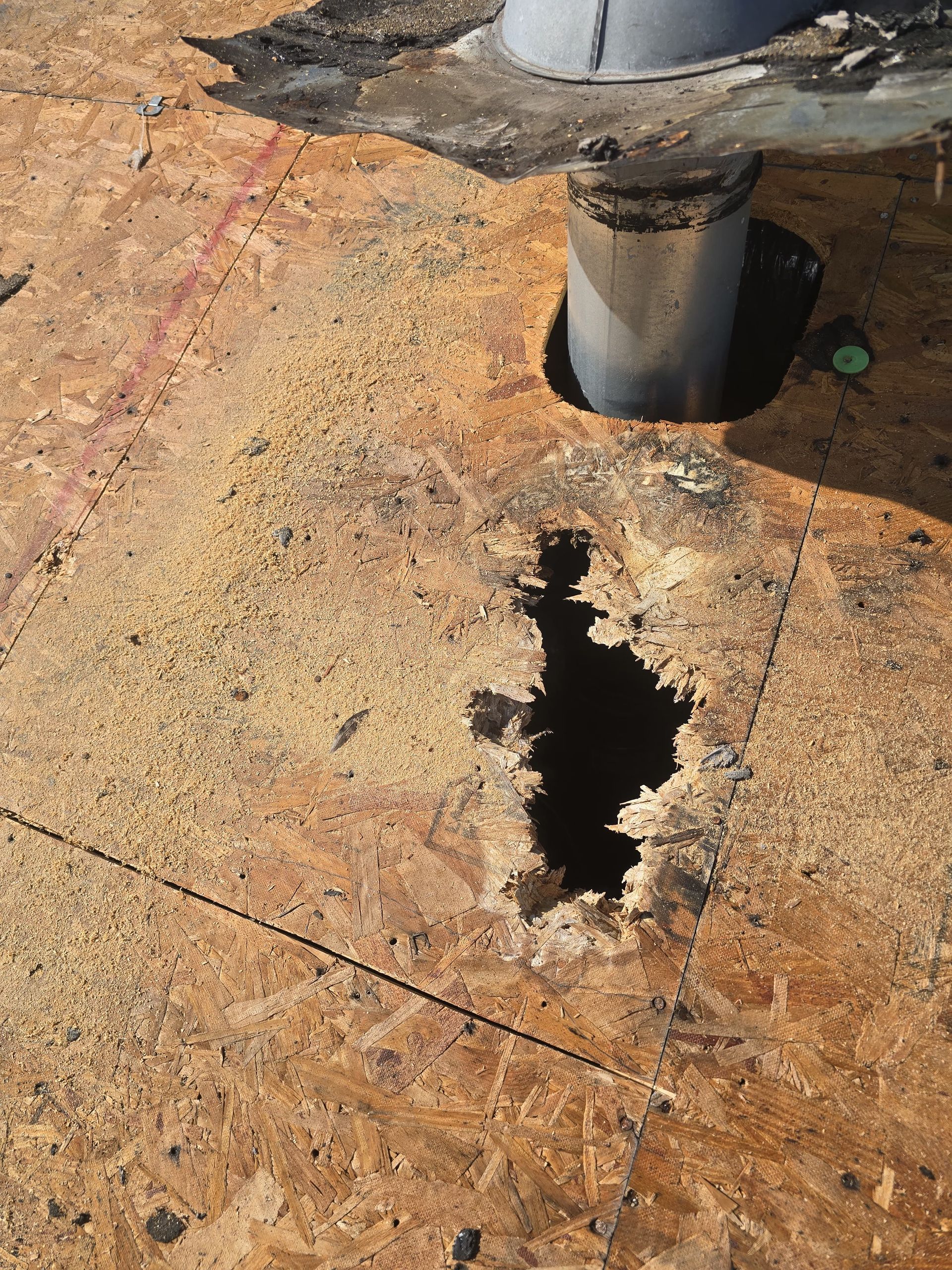 Damaged wood roof with a large hole near a pipe.