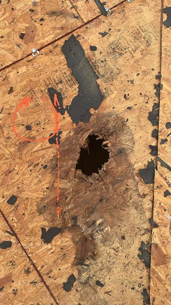 Damaged oriented strand board (OSB) with a large hole and dark staining. Red circle and arrow pointing to area.